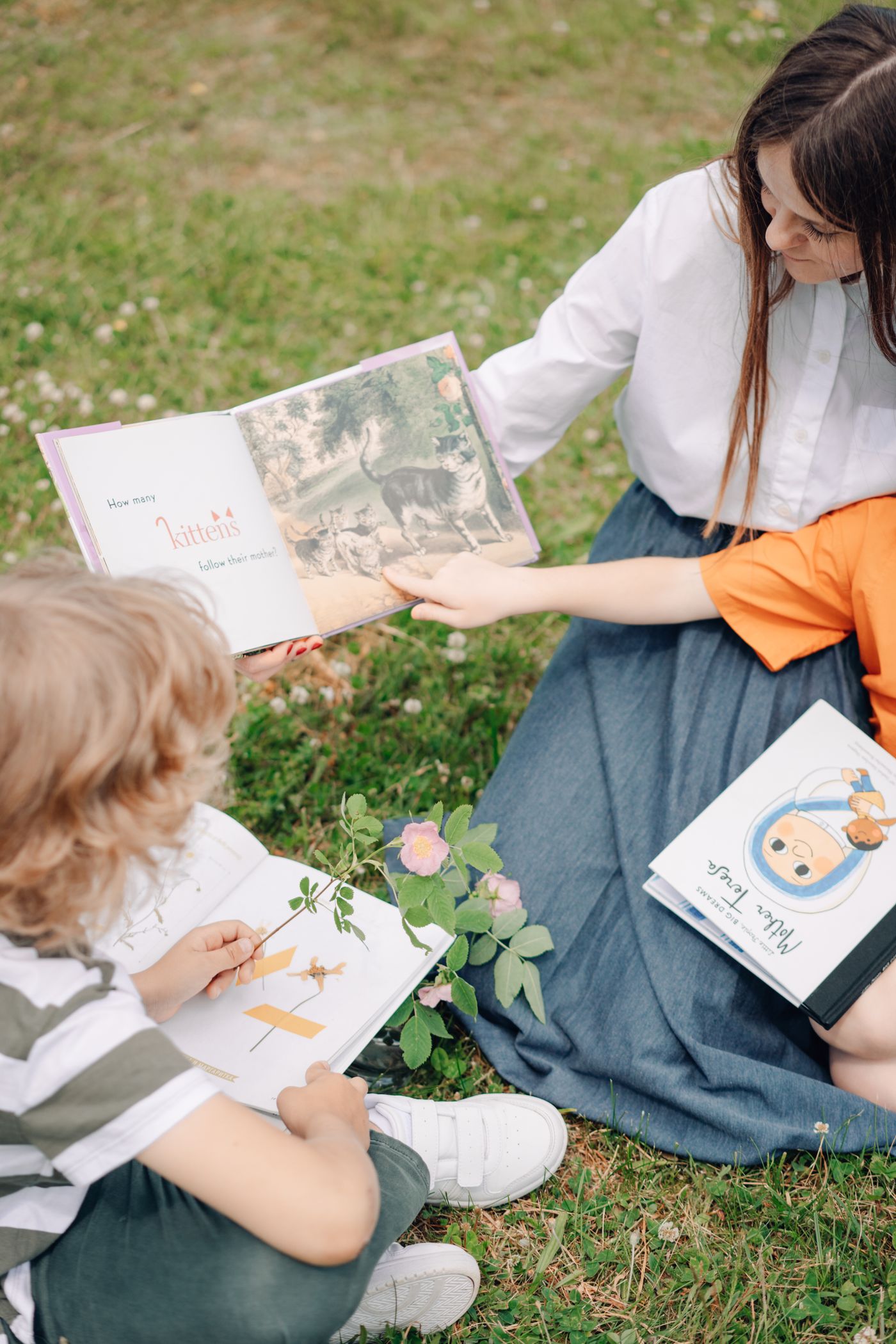 An adult and children reading books together outdoors on the grass.